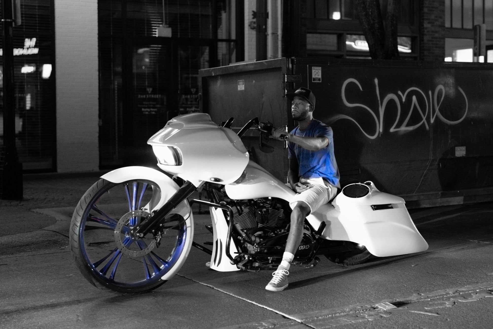 Street portrait of a rider on a custom motorcycle, near-monochrome apart from his blue shirt.