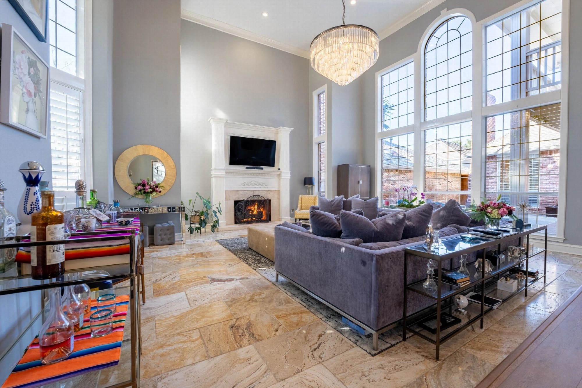 Double-height living room with a chandelier, arched windows and a lit fireplace.