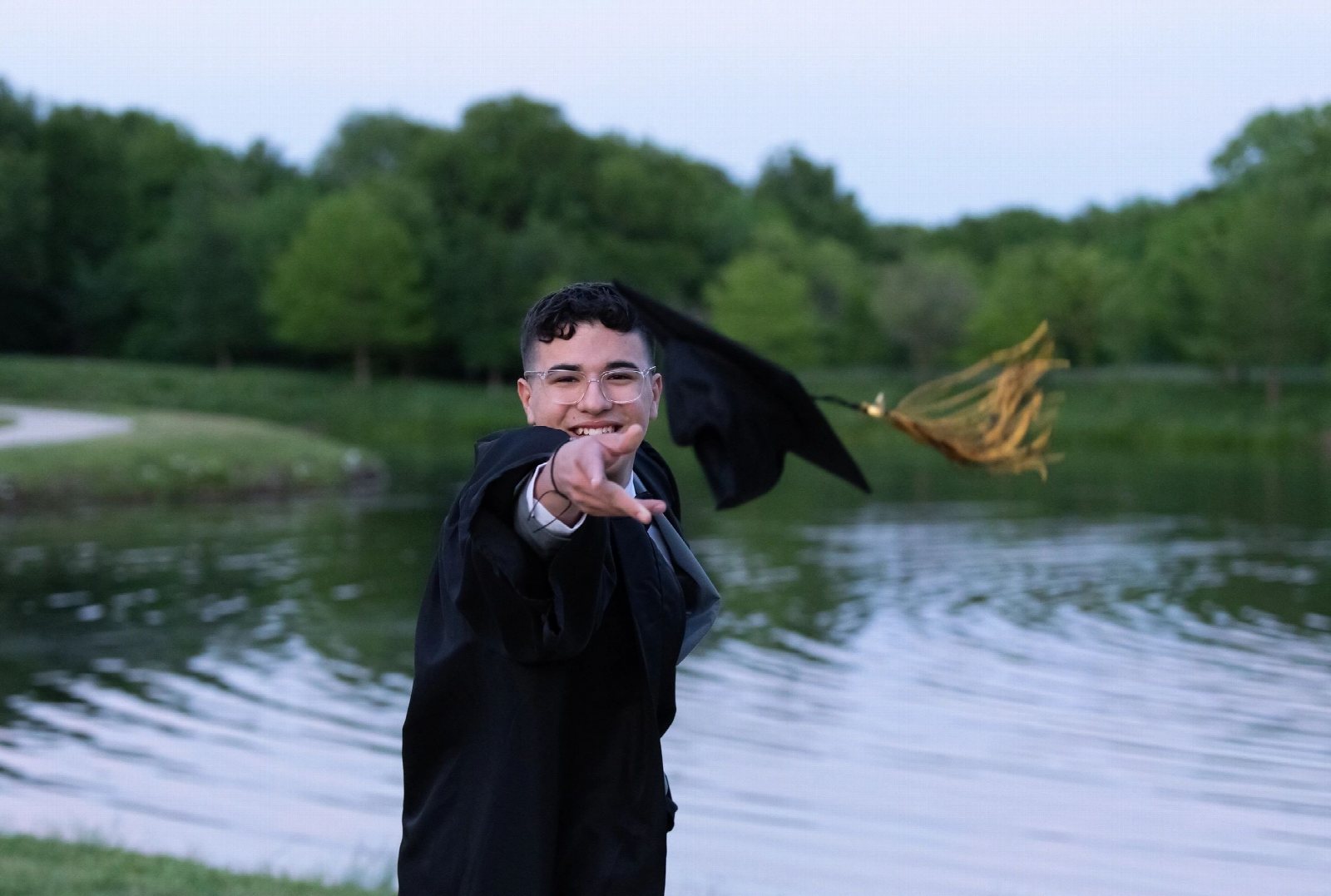 A graduate tossing his cap in the air beside a lake.