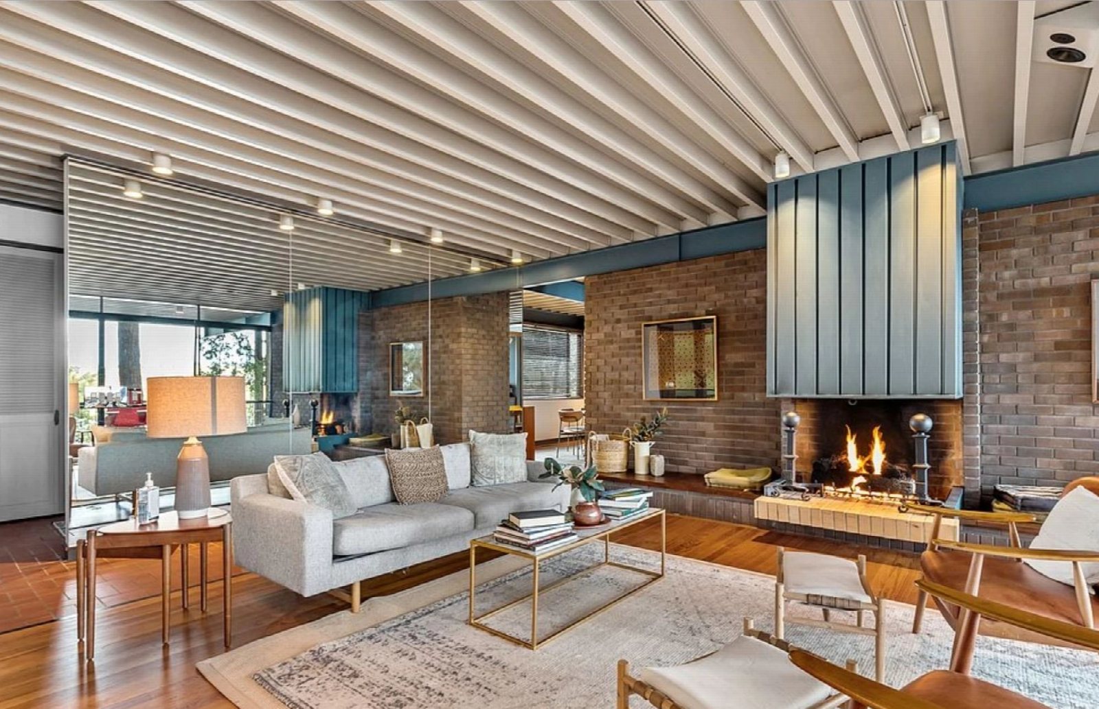 Living room with a brick fireplace wall, a slatted timber ceiling and a full wall of windows.