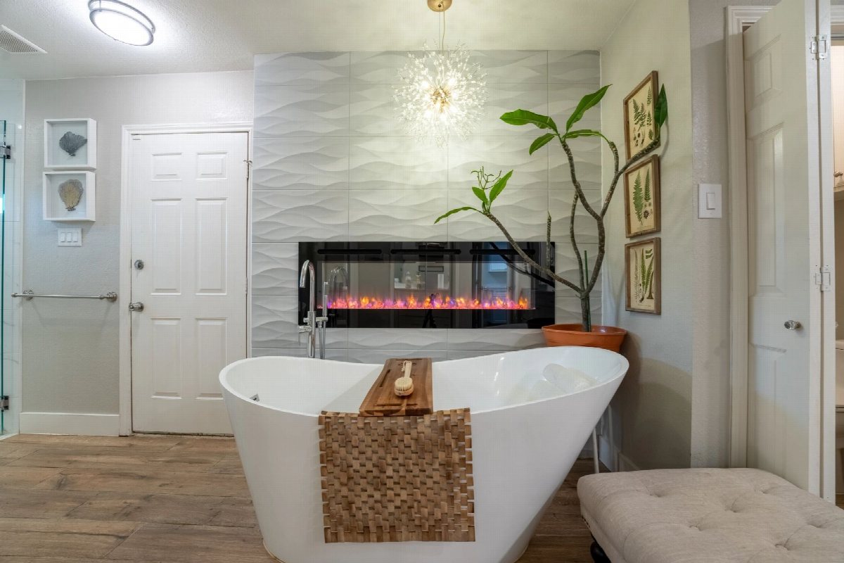 Freestanding bathtub beside a linear fireplace and textured tile wall.